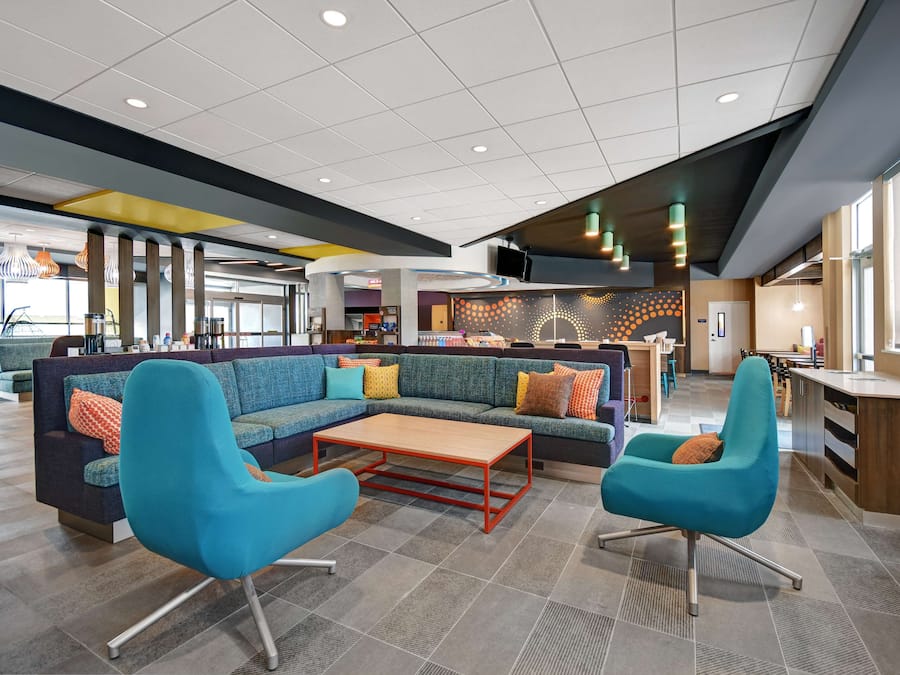 A modern lobby with a sectional sofa, two armchairs, a coffee table, and a kitchen area in the background.