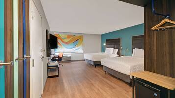 Een hotelkamer met twee bedden, een bureau, een televisie en een kleurrijk abstract schilderij aan de muur.