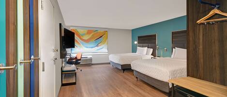 A hotel room with two beds, a desk, a TV, and a colorful abstract painting on the wall.