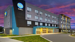 Un moderno edificio de hotel con un llamativo letrero de 'tru by Hilton', varios pisos y una entrada bien iluminada.