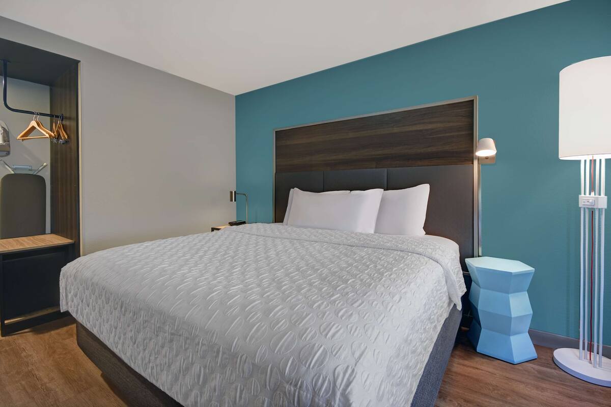 A modern hotel room with a large bed, a nightstand, a wall-mounted lamp, and a blue accent wall.