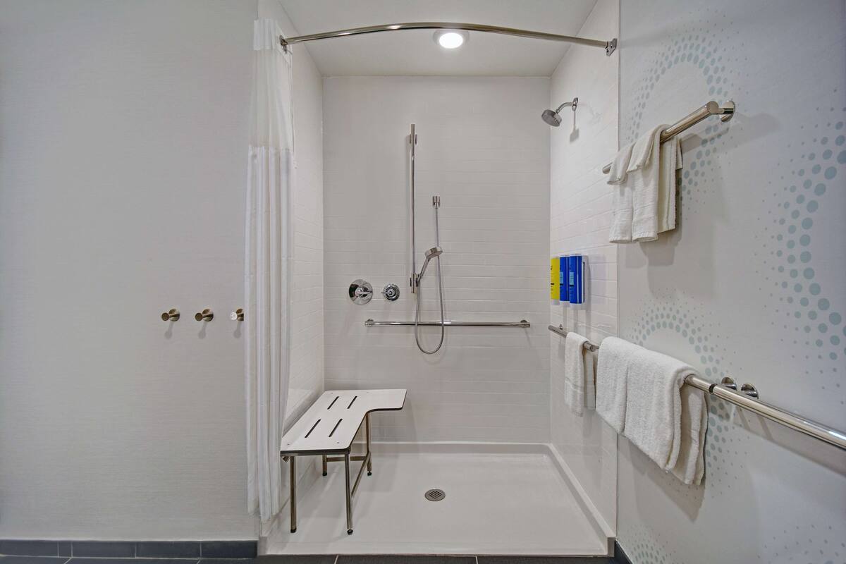 A wheelchair-accessible shower stall with a bench, grab bars, and a towel rack.