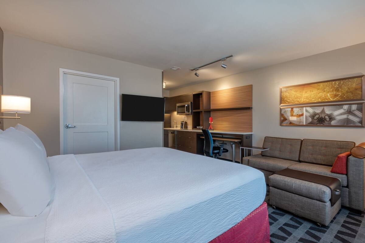 Habitación de hotel con cama, sofá, escritorio, microondas y televisión de pantalla plana.