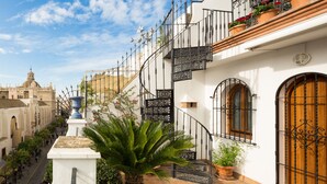 Une vue de rue avec un bâtiment blanc doté d’une porte en bois et de balcons en fer forgé ornés de plantes en pot.