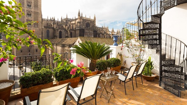 Une terrasse avec des sièges extérieurs, des plantes en pot et une vue sur un bâtiment historique.