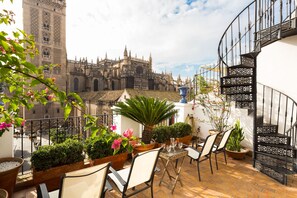 Una terraza con mobiliario exterior, plantas en macetas y vistas a un edificio histórico.