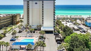 Ein Hochhaus-Hotel mit Pool und Blick auf den Strand, umgeben von Parkplätzen und Palmen.