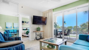 Ein Wohnzimmer mit Fernseher, blau gestreiften Sofas, einem Glastisch und Blick ins Freie.