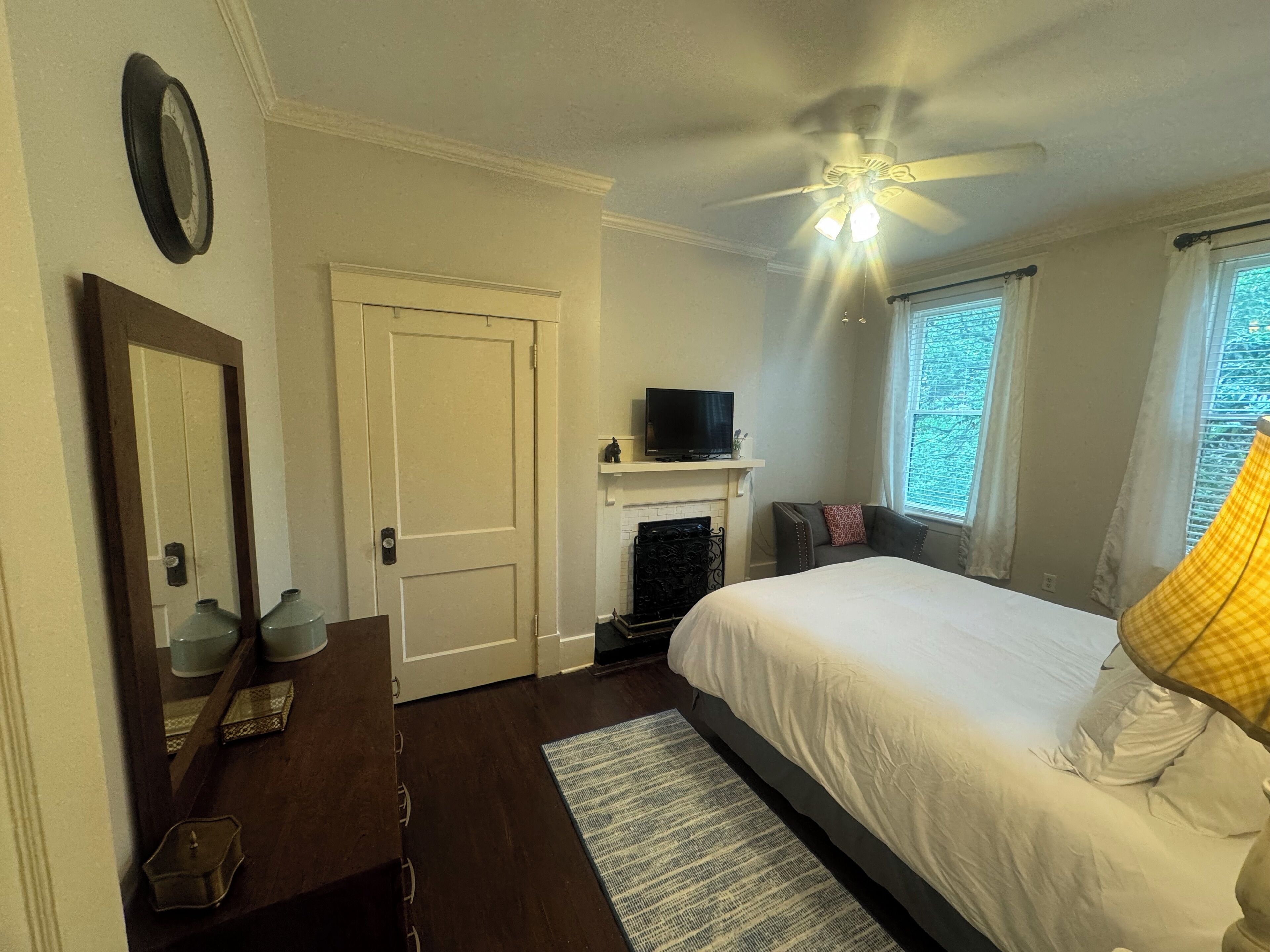 A bedroom with a bed, a ceiling fan, a fireplace, a television, and a window with curtains.