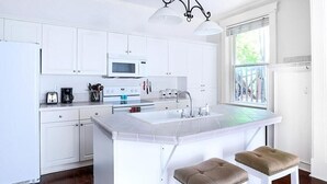 Une cuisine moderne avec des meubles blancs, un îlot central doté de tabourets, un four à micro-ondes et une fenêtre offrant une belle vue.