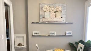 A dining area with a round table, white chairs, a bowl of lemons, and a painting above the shelves. - Forsyth Executive Rental (Savannah)