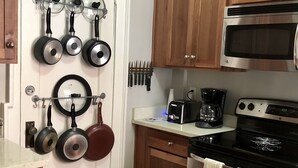 A kitchen with wooden cabinets, a stainless steel oven, a microwave, and pots hanging on the wall. - Forsyth Executive Rental (Savannah)