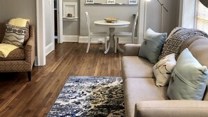 A living room with a sofa, a coffee table, and a dining table with chairs. There is a ceiling fan, a floor lamp, and a painting on the wall. - Forsyth Executive Rental (Savannah)