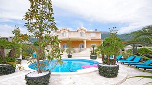 A pool area with a stone floor, surrounded by potted plants and blue lounge chairs. - Luxury Villa Rosalia (Kastela)