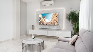 A modern living room with a marble wall, a mounted TV, a round coffee table, a grey sofa, and a large potted plant. - Luxury Villa Rosalia (Kastela)