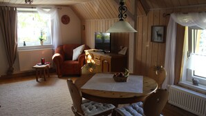 Una habitación acogedora con techo de madera, una mesa redonda con sillas, un sofá, un radiador y una ventana con cortinas.