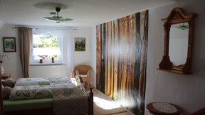 Un dormitorio con cama, ventana con cortinas, un cuadro, una silla y un espejo.