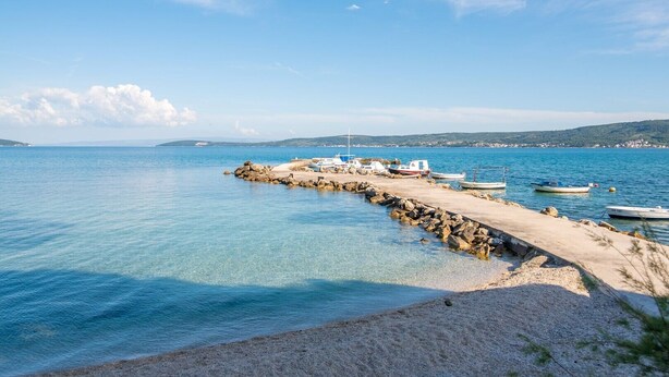 Escena costera con un muelle que se adentra en aguas azules tranquilas, barcos amarrados y cielo despejado.