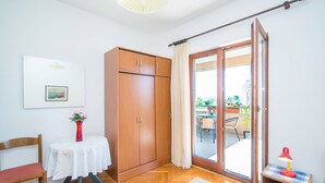 Una habitación con un armario de madera, una mesa con un florero, una silla, una mesita de noche con una lámpara y un ventanal corredero que da a un espacio exterior.