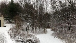En snötäckt stig som leder genom ett skogsområde, med en liten byggnad på vänster sida.