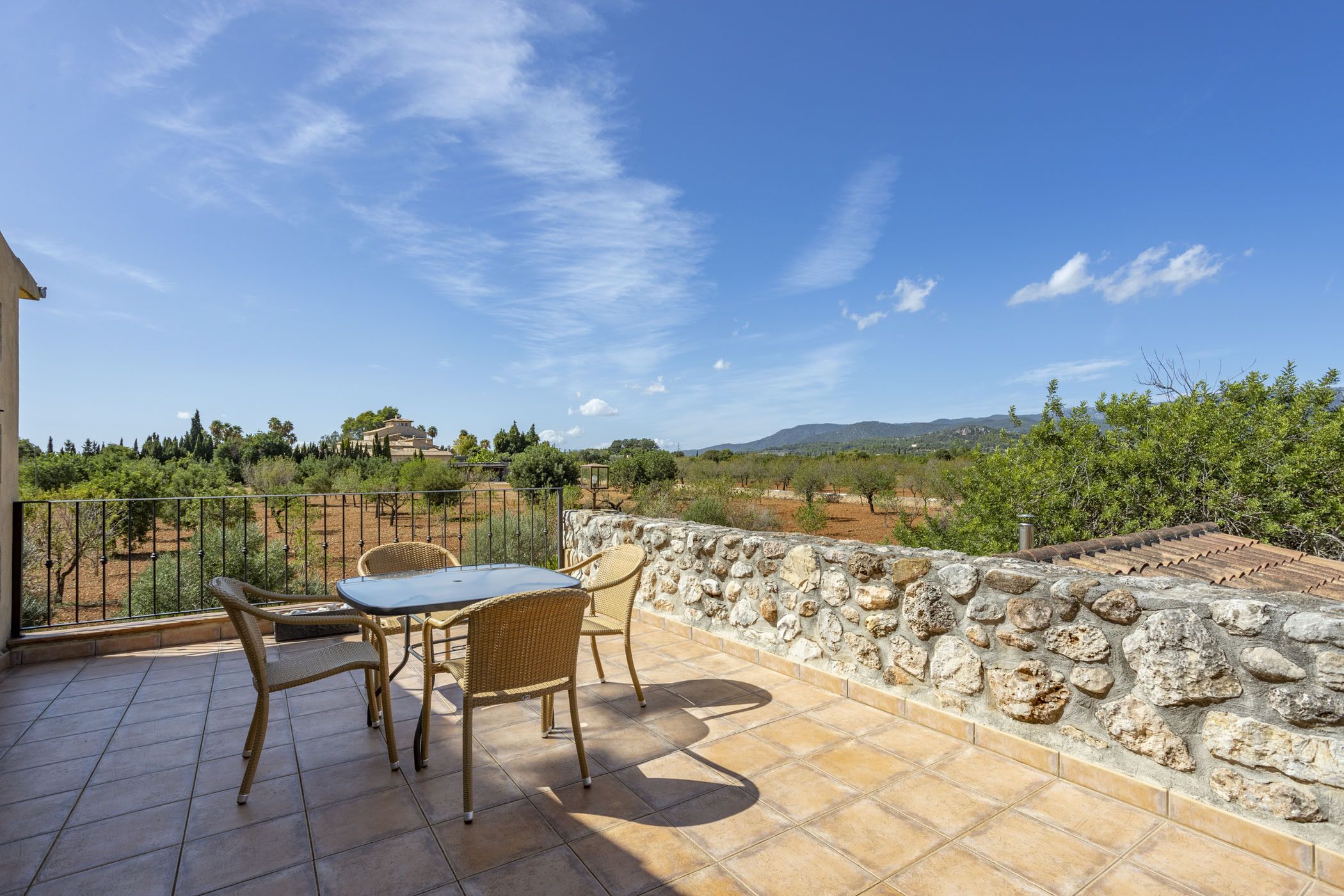 Una terraza con un muro de piedra, una mesa y dos sillas de mimbre.