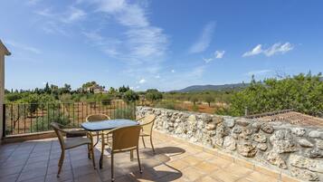 Una terraza con un muro de piedra, una mesa y dos sillas de mimbre.