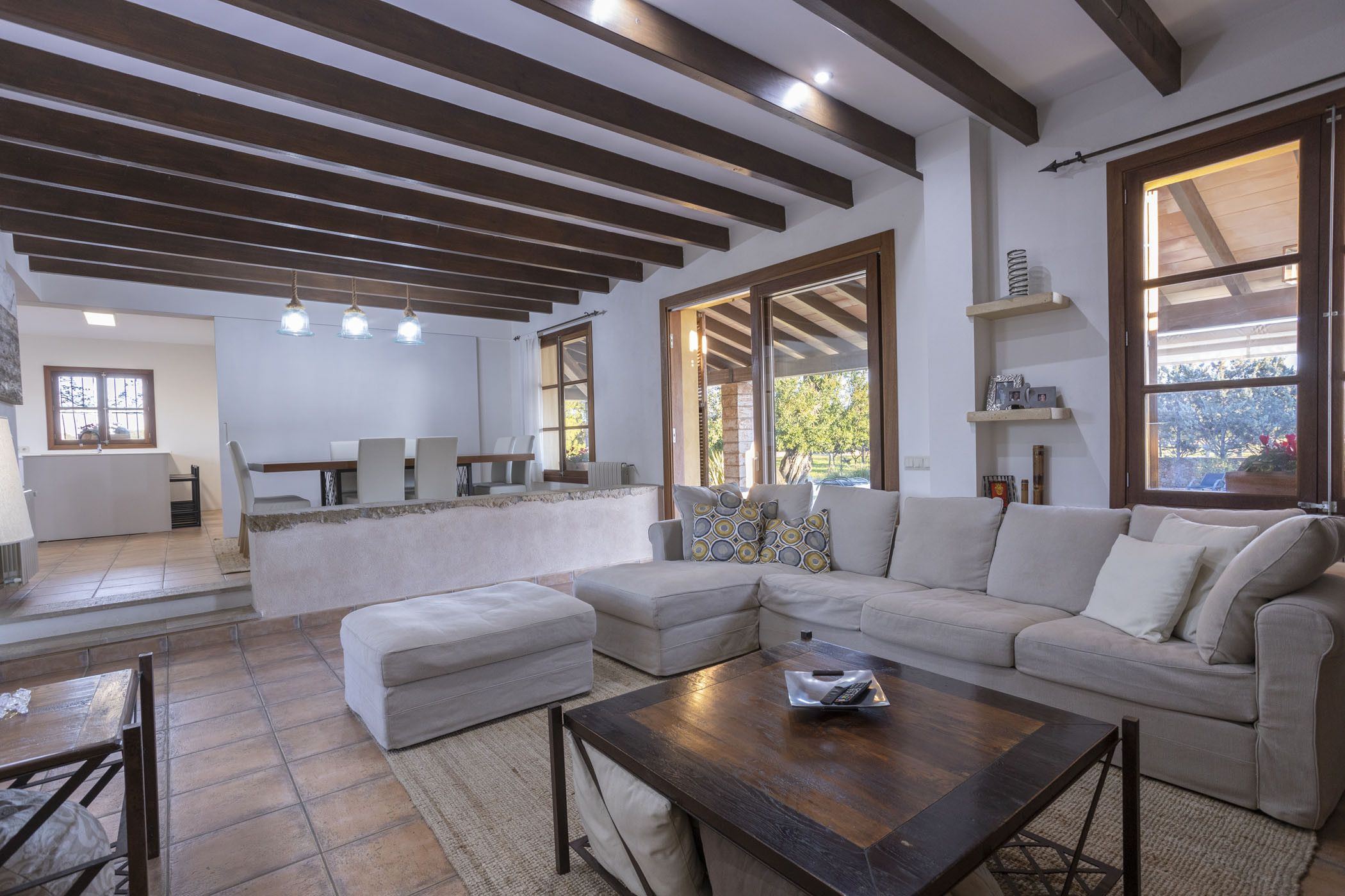 Una sala de estar moderna con un sofá seccional, una mesa de centro de madera y una cocina con un ventanal grande.