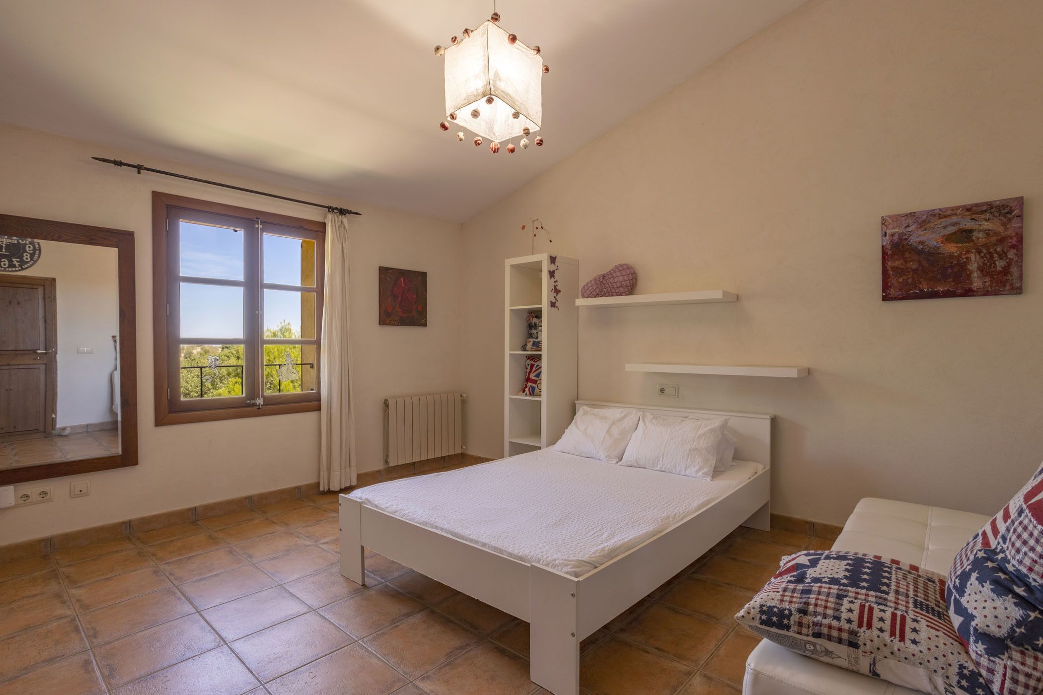 Un dormitorio con cama, ventana, radiador, estante y lámpara colgante.