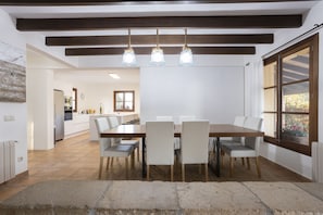 Un coin repas avec une table et des chaises en bois, un sol en pierre et une vue sur la cuisine en arrière-plan.
