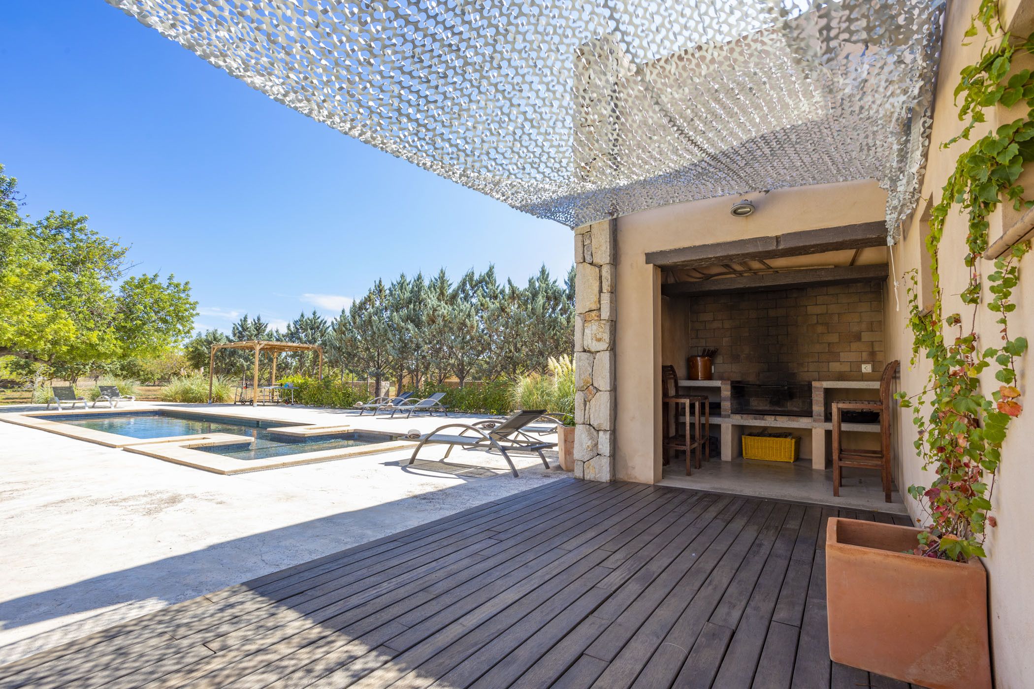 A wooden deck with a pool, outdoor seating, and a stone fireplace.
