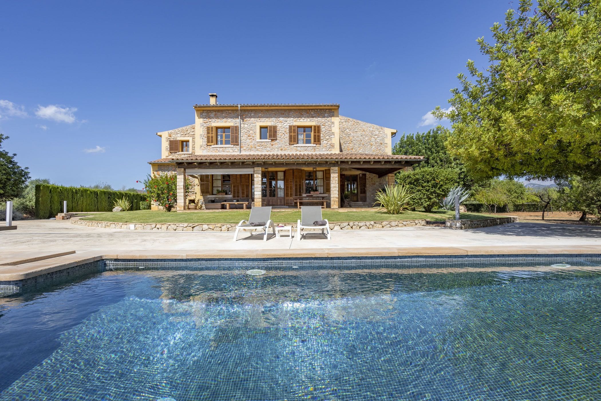 Una amplia casa de piedra con piscina y dos sillones de relax al frente.