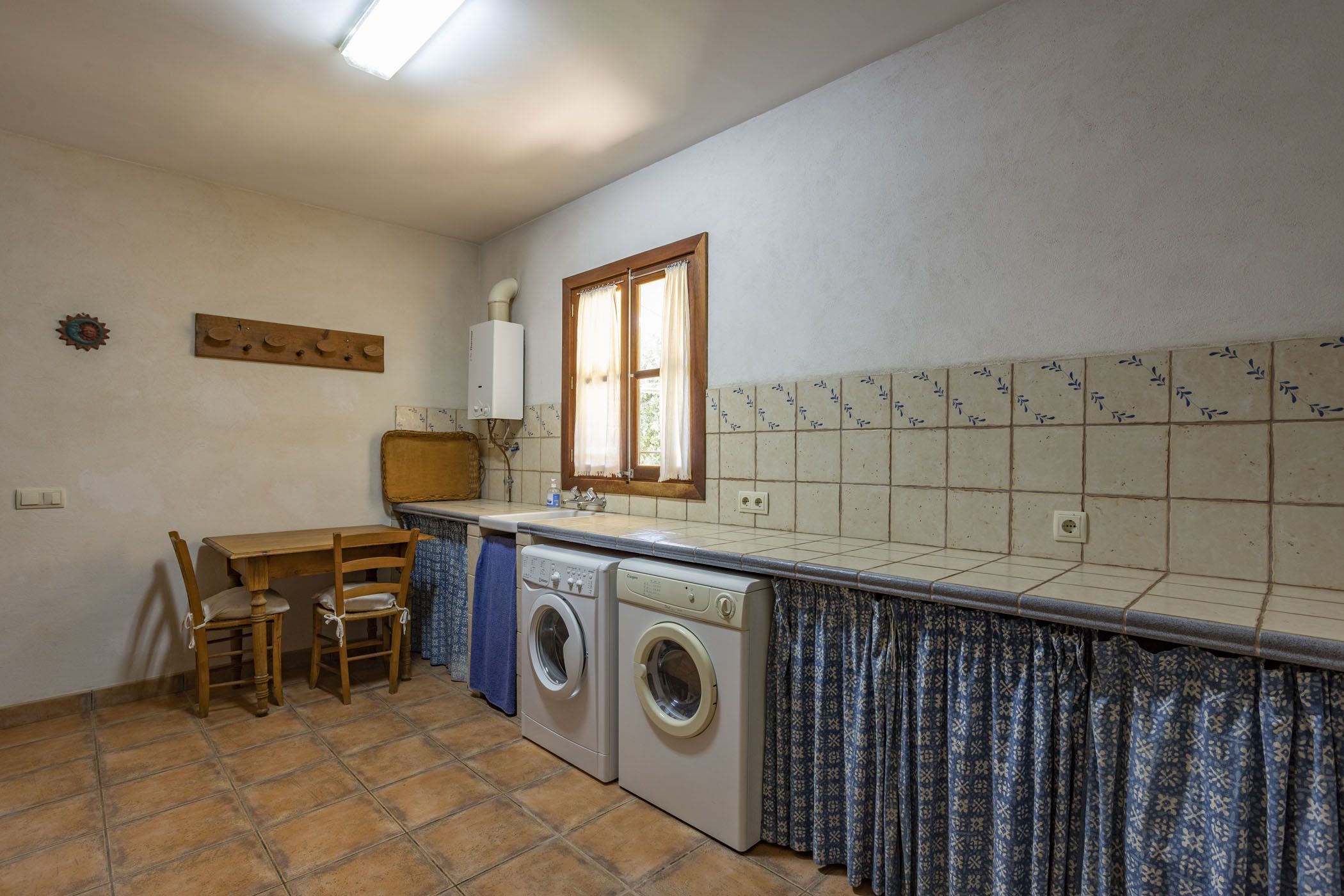 Una cocina compacta con lavadora, una mesa de comedor con sillas y una ventana con cortinas.
