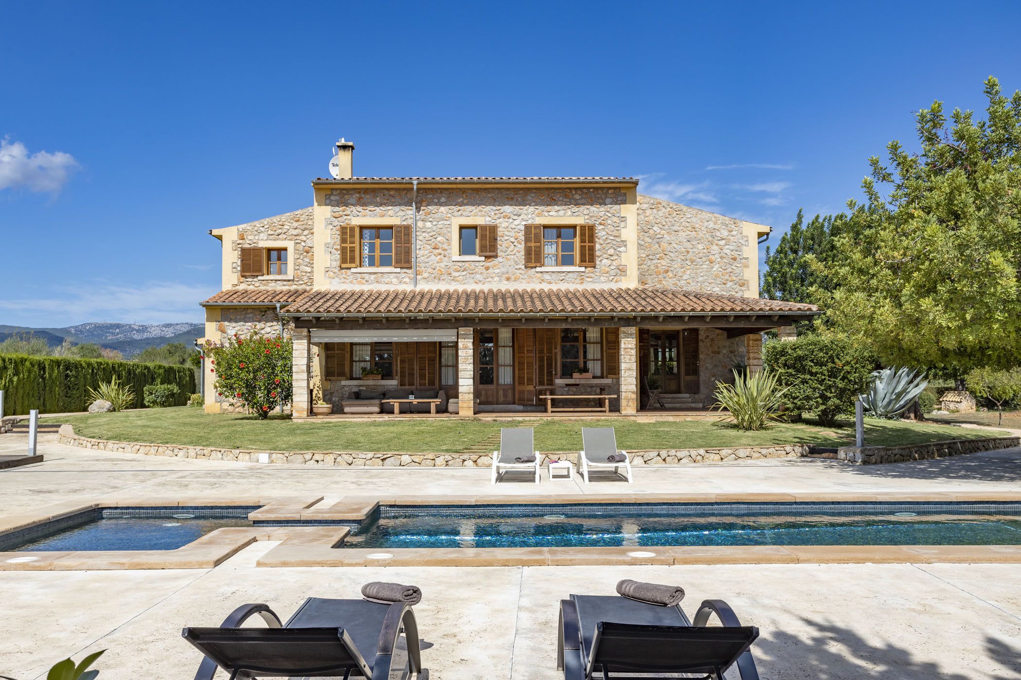 Una casa de piedra de dos pisos con piscina, mobiliario exterior y un césped bien cuidado.