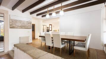 Un comedor con mesa de madera, sillas blancas, un banco de piedra y una lámpara colgante.