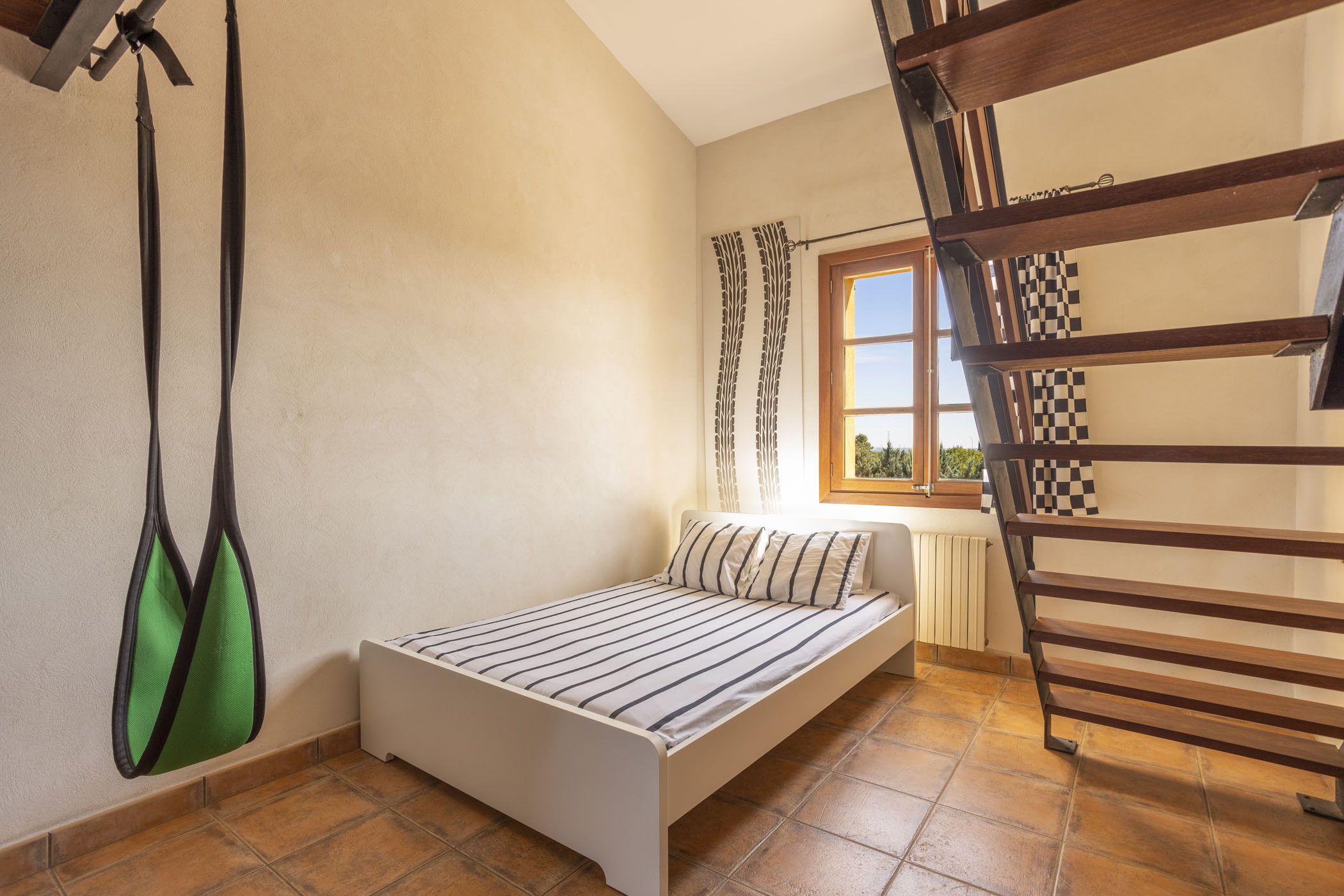 Un dormitorio pequeño con una cama individual, una ventana con cortinas, un radiador y un banco de madera.
