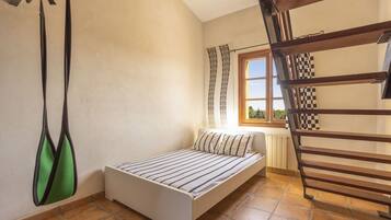 Un dormitorio pequeño con una cama individual, una ventana con cortinas, un radiador y un banco de madera.