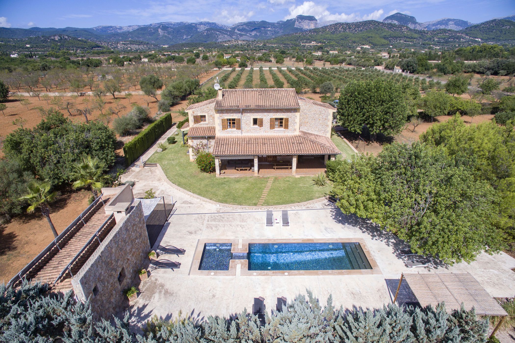 Una amplia casa de piedra con piscina, rodeada por un jardín cuidado y olivares.