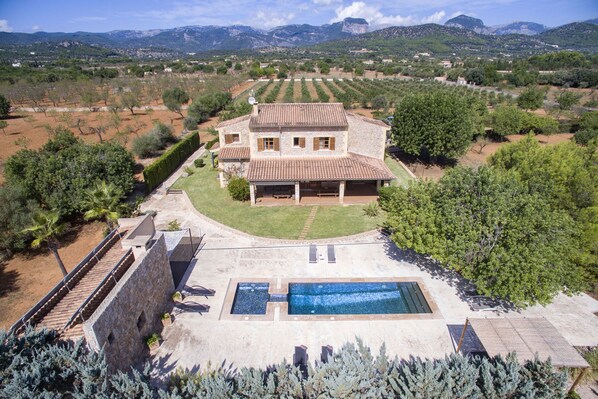 Una amplia casa de piedra con piscina, rodeada por un jardín cuidado y olivares.