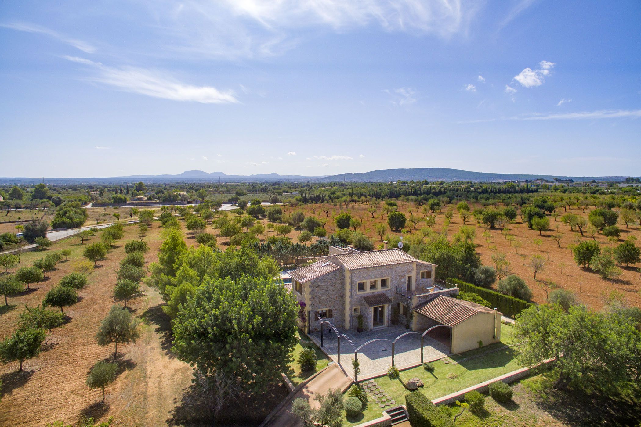 A large, stone building with a tiled roof, surrounded by a well-maintained garden and vineyard.