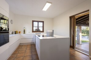 A modern kitchen with white cabinetry, a built-in oven, a sink, and a window with a view of the outdoors. - Fantastic villa with 4 bedrooms, 3 bathrooms, wifi, barbecue, terraces and pool (Binissalem)