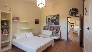 Un dormitorio con cama, un armario blanco, una estantería con almohadas, un reloj de pared y un pasillo que conduce a otra habitación.