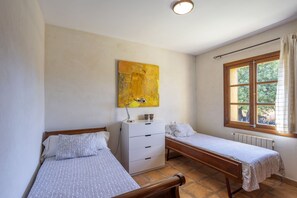 Une chambre avec deux lits simples, une commode blanche, un tableau abstrait jaune et une fenêtre donnant sur un paysage verdoyant.