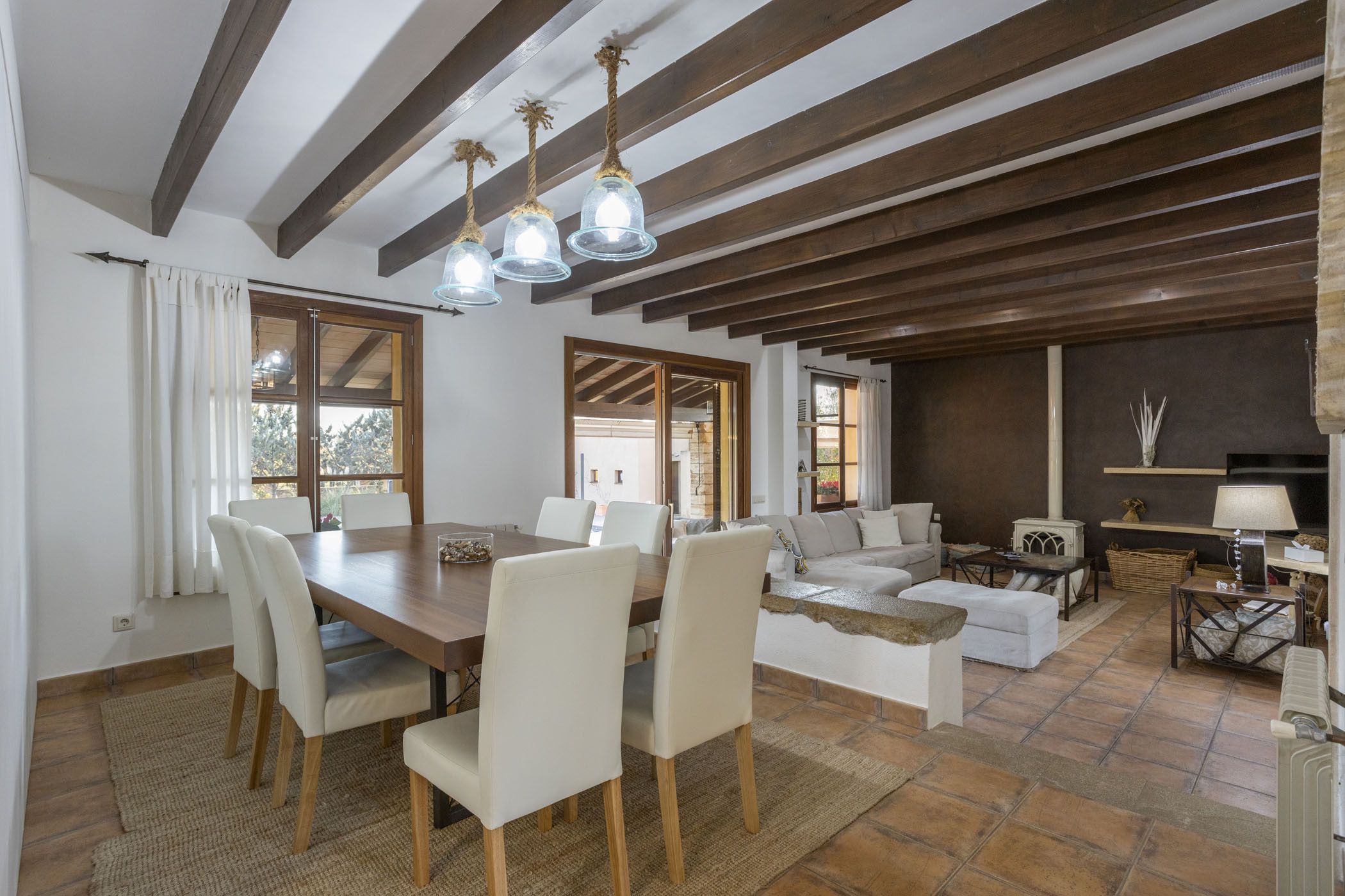 Amplia sala de estar con una mesa de comedor de madera, sillas blancas, un sofá y una chimenea.
