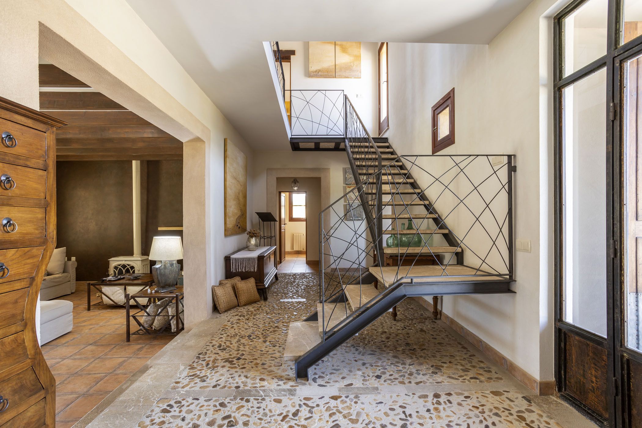 Un interior espacioso con una escalera, un mueble de madera, una lámpara y un suelo con diseño.