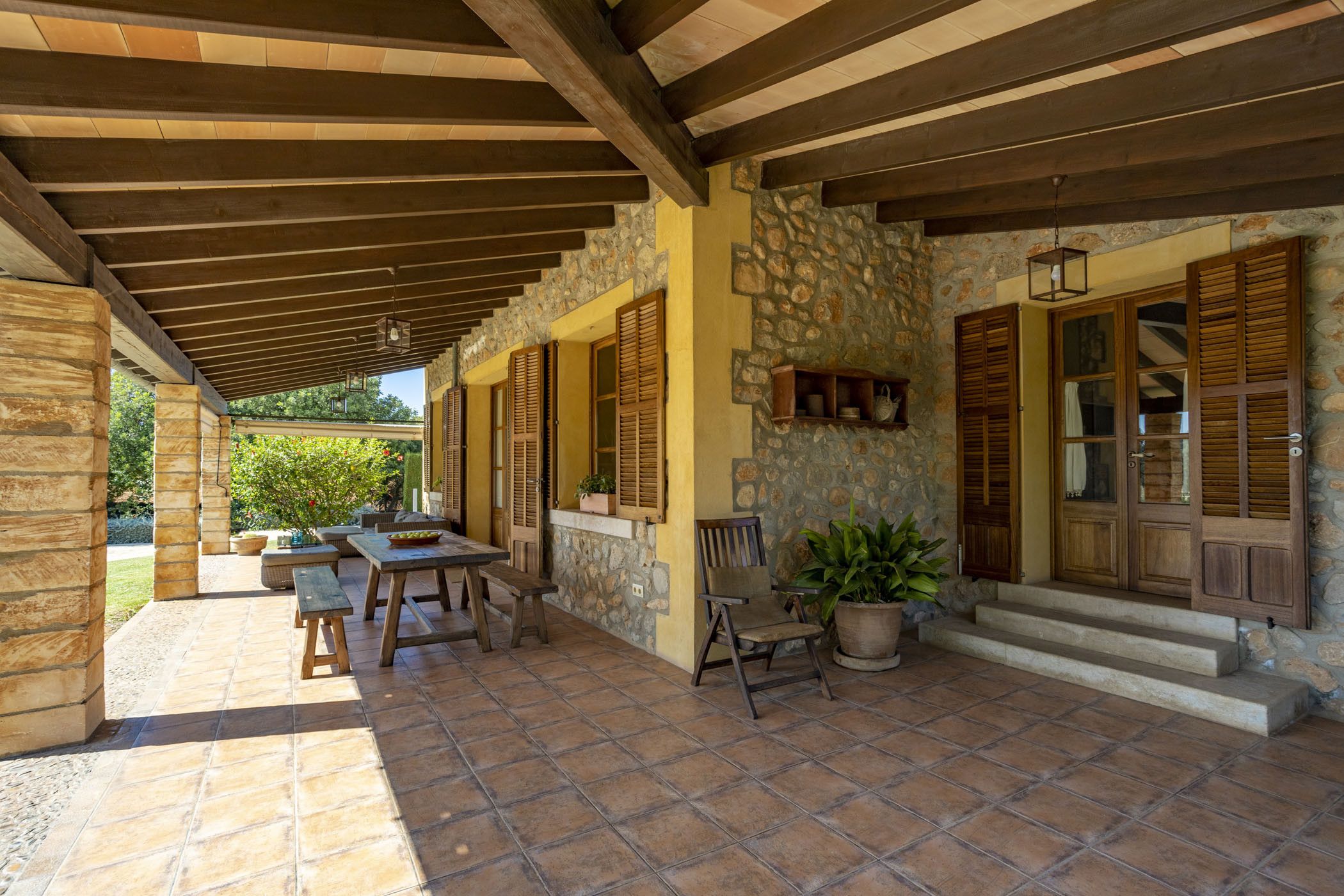 Un patio cubierto con paredes de piedra, contraventanas de madera y un banco de piedra.