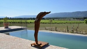 A sculpture by a pool with a clear view of vineyards and mountains in the background. - Merlot (Robion)