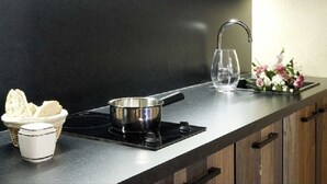 A kitchen with a black countertop, a stainless steel pan, a white mug, a basket of bread, and a vase with flowers. - Merlot (Robion)