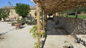 A covered outdoor area with a stone wall, a pergola, and a gravel path leading to a building. - Merlot (Robion)