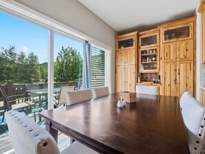 Uma área de refeições com uma mesa grande, cadeiras e armários de madeira com portas de vidro.