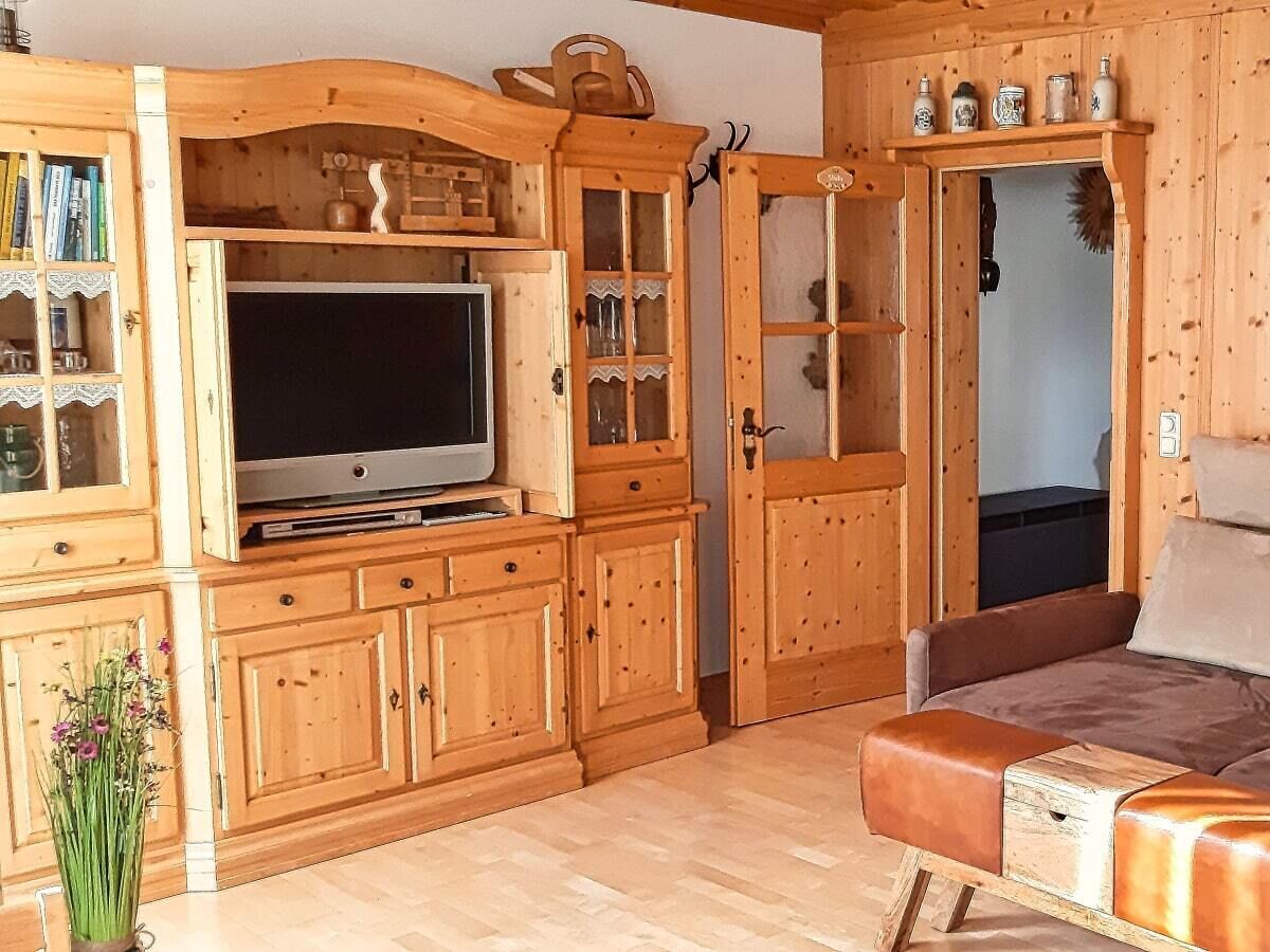 L’intérieur d’un chalet en bois, avec un téléviseur, des meubles en bois, un canapé et une porte donnant sur une autre pièce.